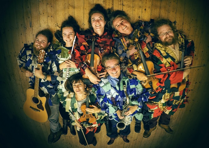 Musicians dressed in English traditional clothing holding their instruments lying in a group on the floor grinning