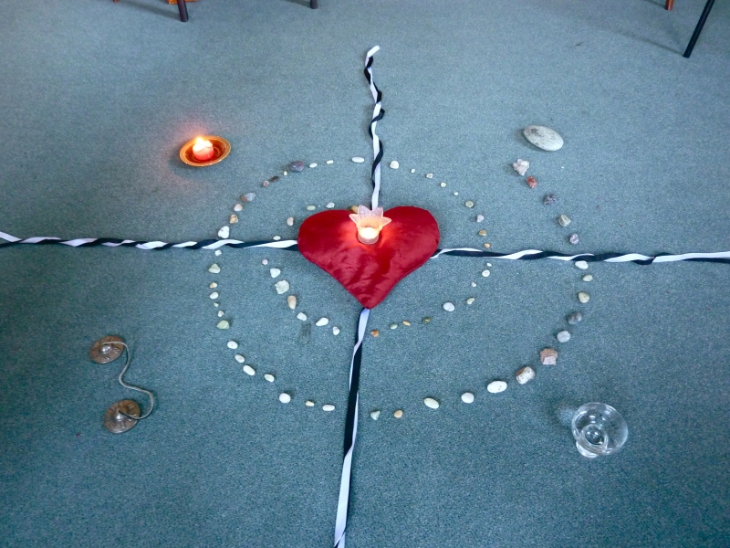 Mandala on the floor, heart, cross and spiral centre, with candle, shell, temple bell and oil