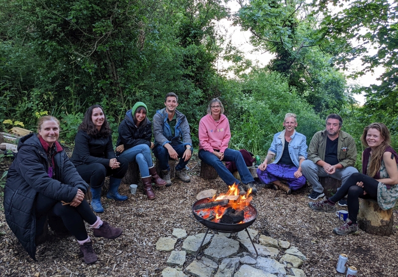 Young adults sat round a fire pit in the woods